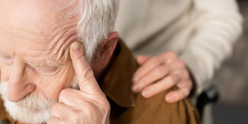 Elderly man on a wheelchair with his finger on his temple