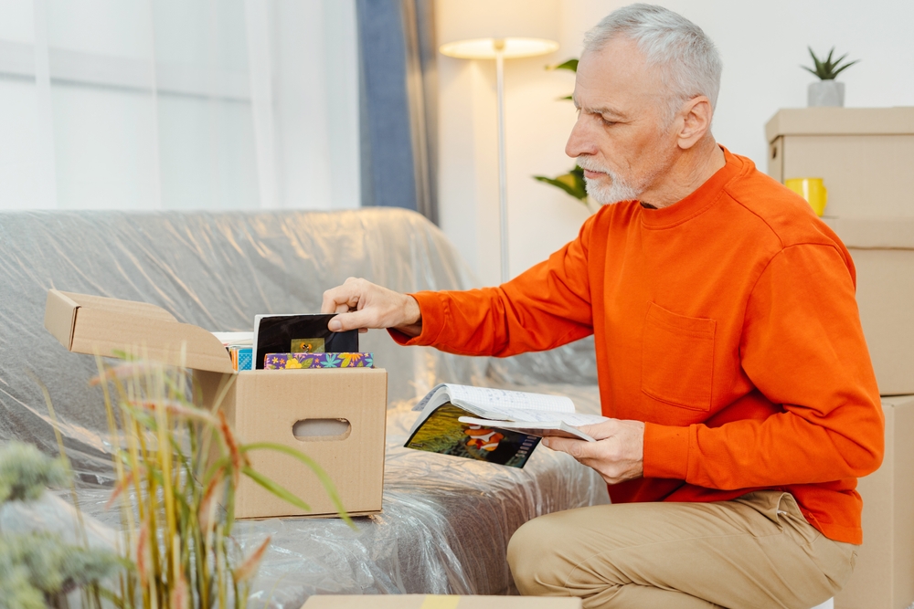 Senior,Man,Examining,Belongings,While,Unpacking,Cupboard,Boxes,At,New