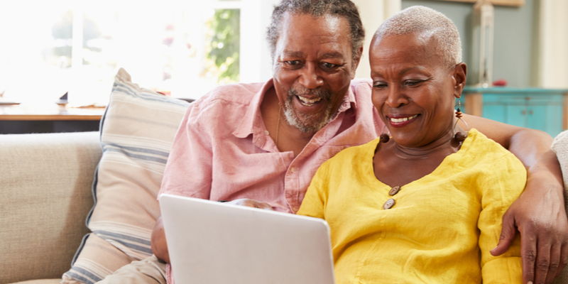 What Is The Role Of Technology In Memory Care? Senior couple smiles at computer screen